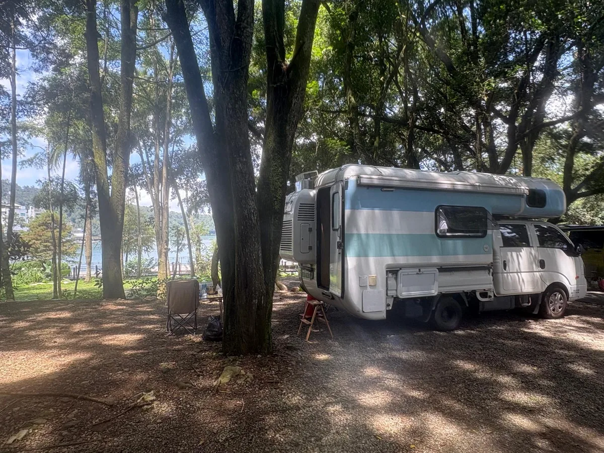 藍白露營車停在台灣綠意森林營區，展示國際旅客可依行程選擇山林、海岸或湖畔營地