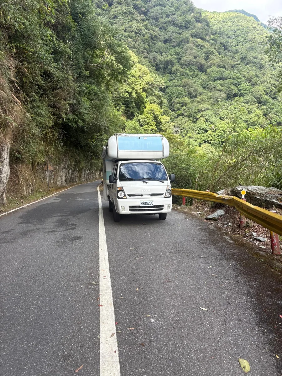 藍白露營車行駛在中部橫貫公路與合歡山一帶的狹窄山路，周圍是峭壁與森林