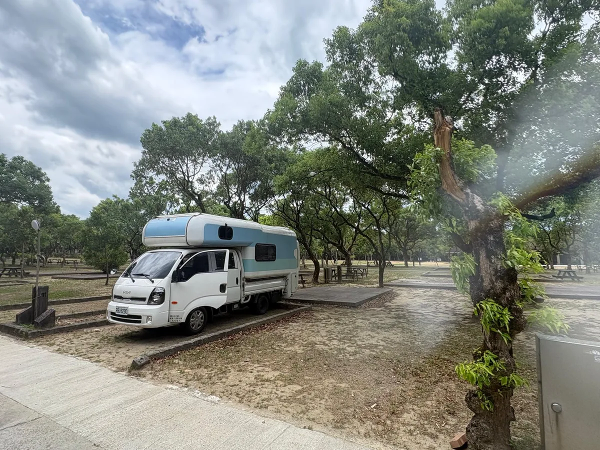 藍白露營車停靠在台灣公路旁的大樹下，呈現國際旅客自由安排休息節奏的公路旅行日常