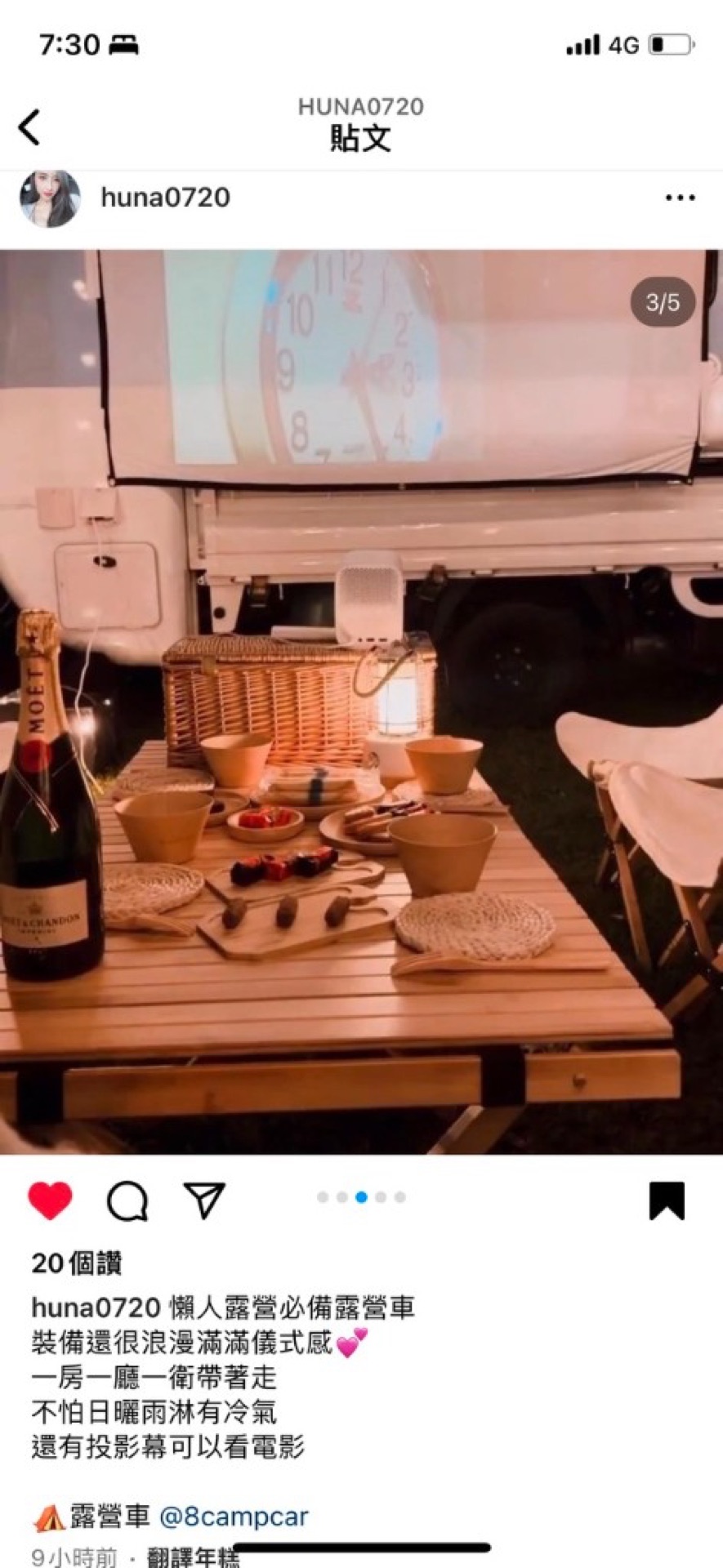 Wood picnic table champagne wooden plate snacks lantern, mini projector on white campervan side screen, night grass refined lazy glamping group dinner mood