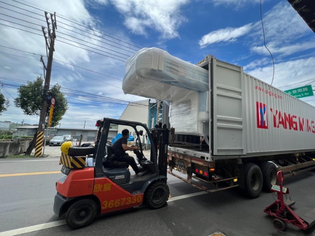 Joyforest build diary: forklift unloading wrapped campervan body module from ocean container, outdoor unload under blue sky