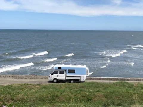 露營車停在開闊海岸線旁，前方是海浪與長長的海平面