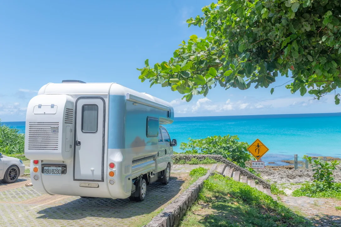 露營車停在海邊樹蔭下，右側階梯可直接通往海岸