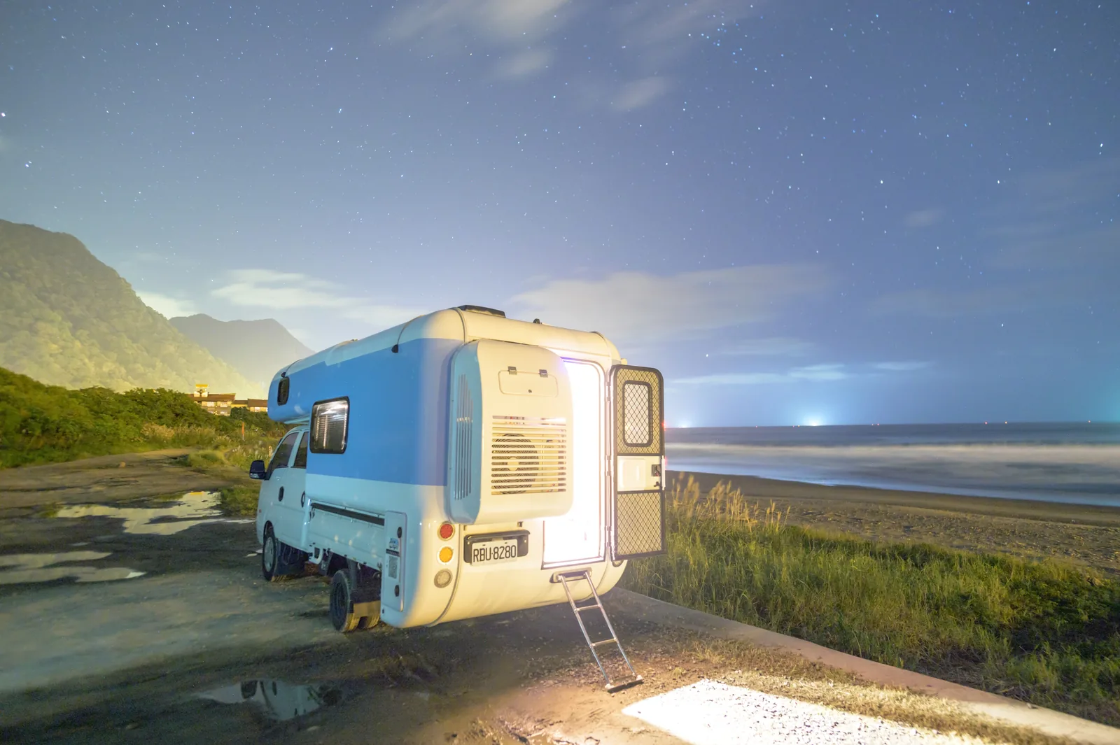 露營車停在山與太平洋之間，夜空佈滿星星，車門亮著溫暖燈光